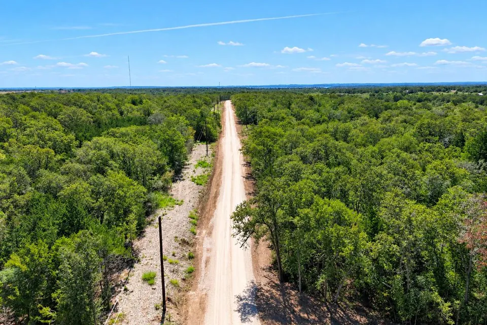 Aerial view of a graded dirt road and overhead power line running through wooded rural land
