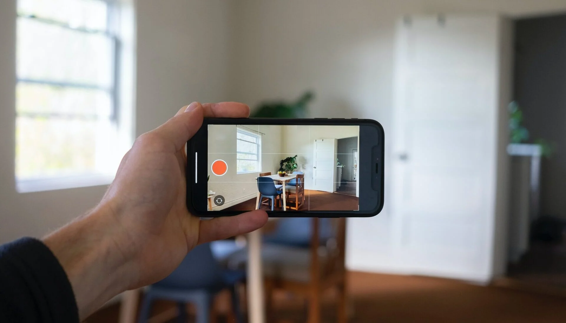 Hand holding a smartphone to photograph an empty room