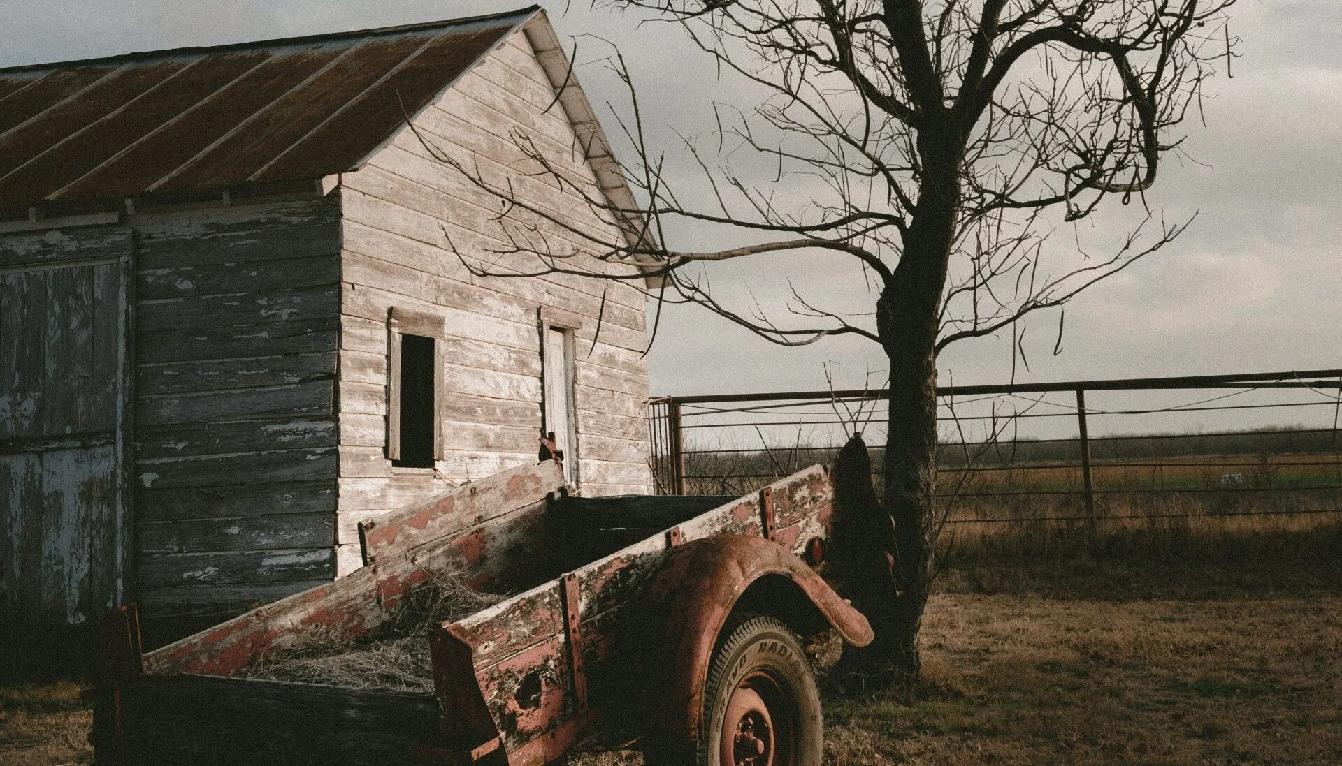 Weathered wooden house beside a leafless tree and an old cart
